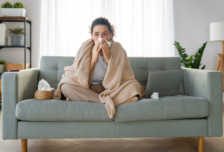 Prehlađena žena sedi na kauču prekrivena ćebetom